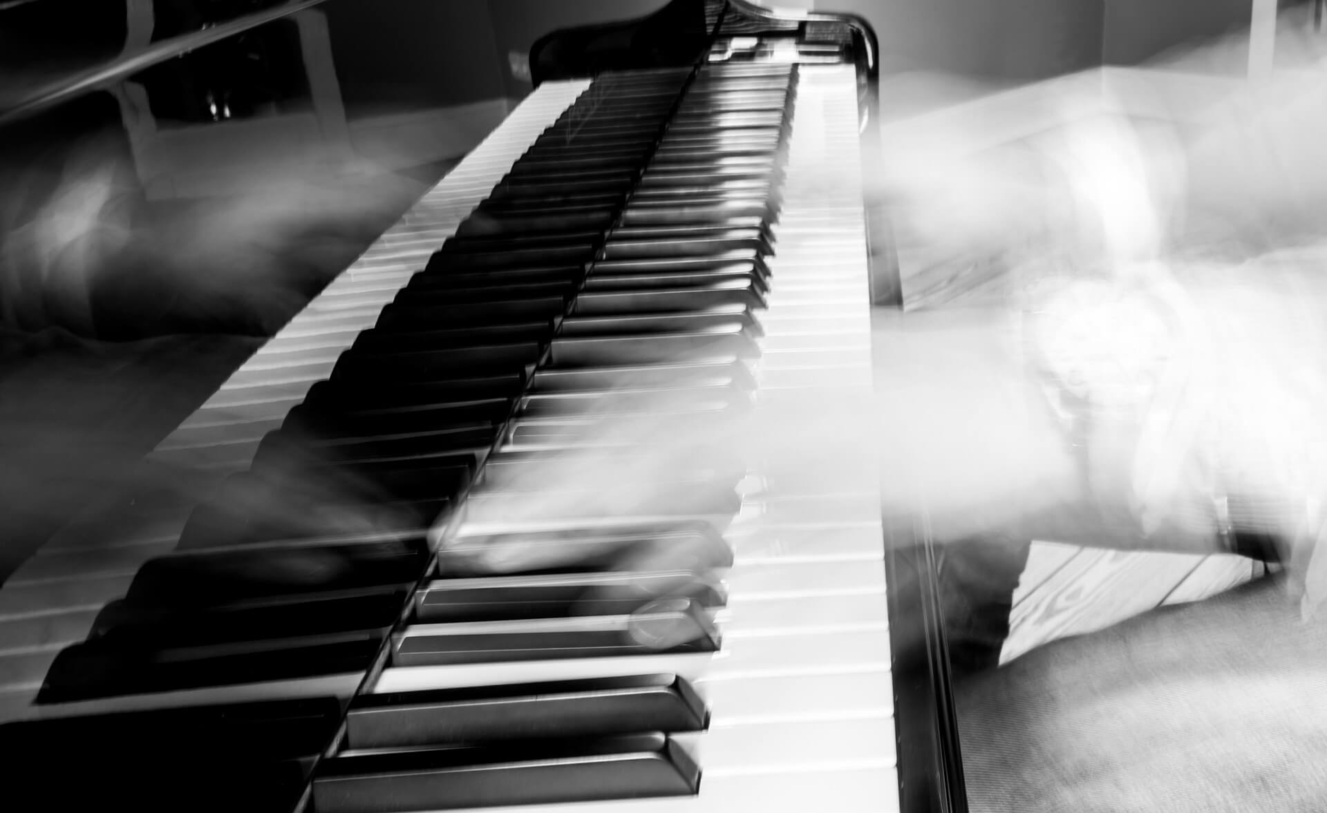 Pianisti soittamassa pianoa mustavalkoisessa kuvassa. Elävä pianomusiikki tuo tunnelmaa juhliin, yritystapahtumiin, häihin ja muihin tilaisuuksiin.