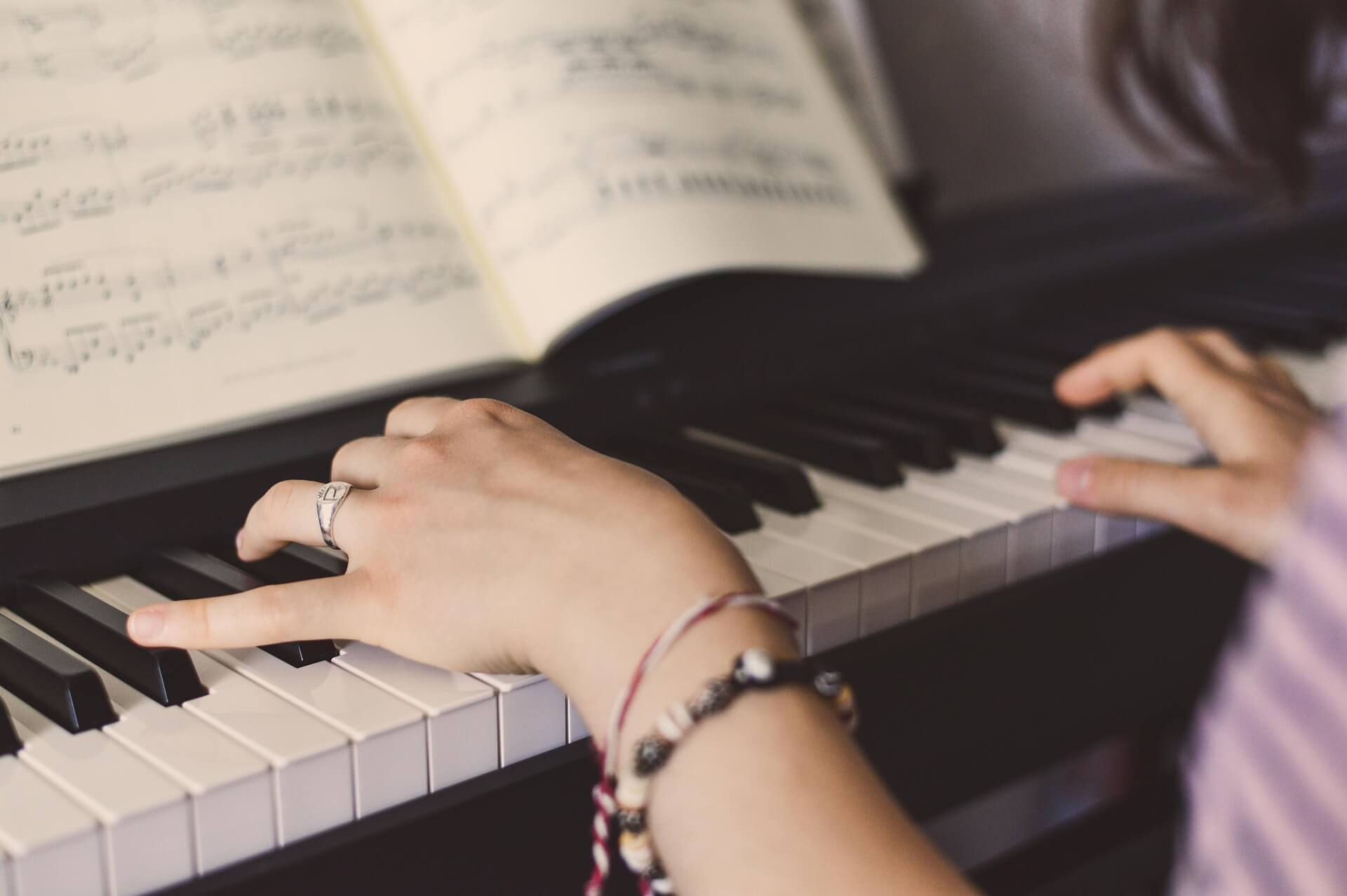 Aloittelija harjoittelemassa pianonsoittoa pianolla nuottien avulla.